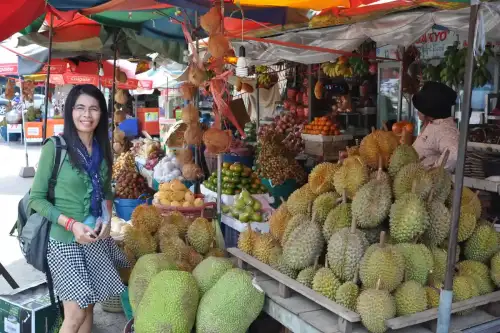 Exploring Gluten-Free Fettuccine Made with Jackfruit, Rice, and Tapioca Flour - Malin smiles next to a stall selling durian and jackfruit by shankar s. is licensed under CC BY 2.0.